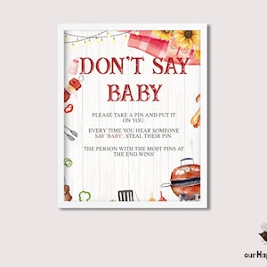 Op de afbeelding: Een wit bord met een rood-wit geruite achtergrond en een rode rand. Het bord zegt "Don't Say Baby" en bevat instructies voor een spel. De instructies zeggen om een ​​pin te nemen en deze op jezelf te bevestigen, elke keer dat je iemand "baby" hoort zeggen. De persoon met de meeste pinnen aan het einde wint.