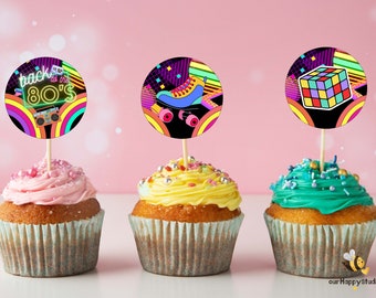 Op de afbeelding: Drie cupcakes versierd met kleurrijke sprinkles en bedekt met ronde, neonkleurige papieren cirkels. De cirkels bevatten 80s-themaontwerpen, waaronder een rolstoel, een Rubik's Cube en de tekst "back to the 80's".