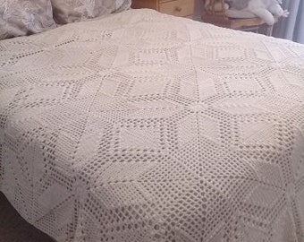Puede incluir: Colcha de cama de crochet blanco con un patrón de diamante. La colcha está sobre un marco de cama de madera con almohadas blancas.