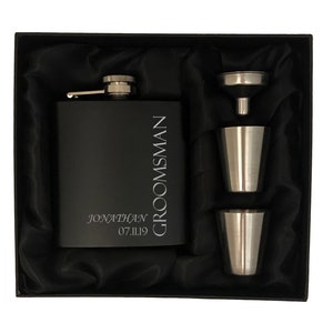 May include: Black gift box containing a black hip flask, two shot glasses and a funnel. The flask is engraved with the text "GROOMSMAN JONATHAN 07.11.19".