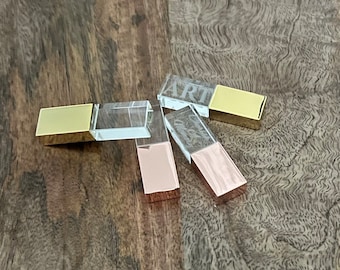May include: Three crystal USB flash drives with gold and rose gold metal caps. The drives are engraved with the word "ART".