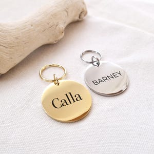 Peut inclure: Deux m&eacute;dailles d'identification rondes en m&eacute;tal pour animaux de compagnie avec des anneaux. La m&eacute;daille dor&eacute;e indique "Calla" et la m&eacute;daille argent&eacute;e indique "Barney".