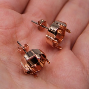 Könnte beinhalten: Zwei Ohrringfassungen aus Roségold mit Zinken zum Einsetzen von Steinen. Die Fassungen liegen auf einer Hand.