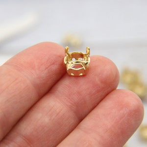 Pode incluir: Engaste de metal dourado para uma pedra preciosa ou cabochão. O engaste tem uma abertura redonda e um design decorativo.