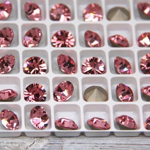 May include: A close-up of a white plastic tray filled with pink rhinestones. The rhinestones are arranged in rows and columns, and they are all the same size and shape.