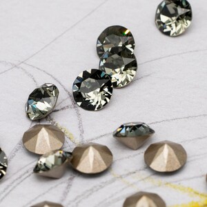 May include: A collection of silver and black rhinestones on a white surface with a yellow and orange background.