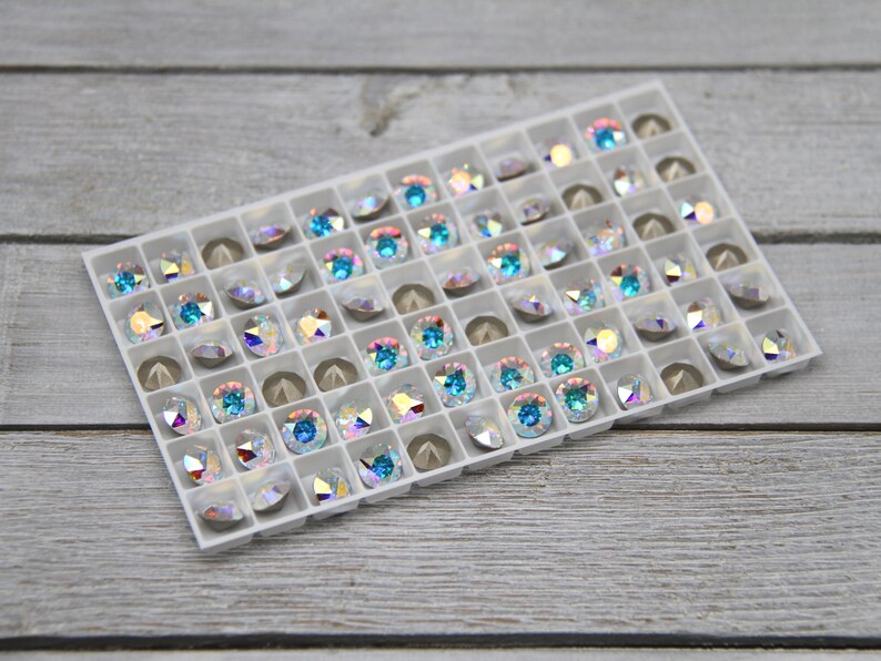 May include: A white plastic tray filled with iridescent blue and clear rhinestones. The rhinestones are arranged in a grid pattern.