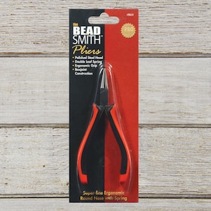 May include: The Bead Smith round nose pliers with a polished steel head, double leaf spring, and ergonomic black and orange handles. The tool is packaged on a black and red card featuring the text The Bead Smith Pliers, Pro Quality, and ER854.