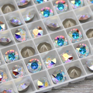 May include: A white plastic tray filled with small, iridescent, round rhinestones. The rhinestones are arranged in rows and columns, and some are a light blue colour.
