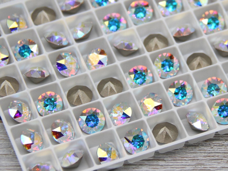 May include: A white plastic tray filled with small, iridescent, round rhinestones. The rhinestones are arranged in rows and columns, and some are a light blue colour.