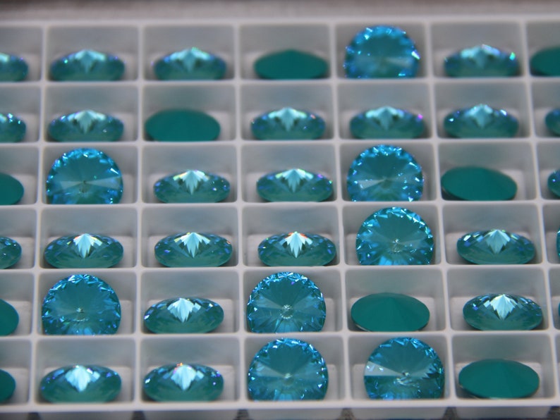 Pu&ograve; includere: Un vassoio pieno di strass color turchese. Gli strass sono di diverse forme, tra cui rotondi, ovali e a semicerchio. Il vassoio &egrave; diviso in piccoli scomparti quadrati, ognuno contenente un singolo strass. Gli strass hanno una superficie sfaccettata che riflette la luce.