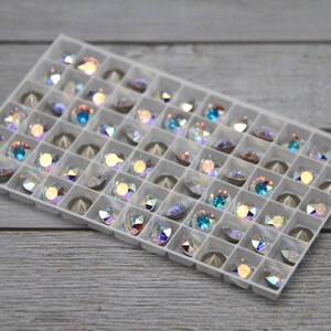 May include: A white plastic tray filled with iridescent and blue rhinestones. The rhinestones are arranged in a grid pattern.