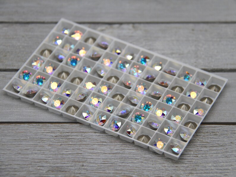 May include: A white plastic tray filled with iridescent and blue rhinestones. The rhinestones are arranged in a grid pattern.