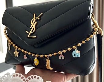 Puede incluir: Bolso de hombro acolchado negro con un logotipo YSL dorado y una correa de cadena dorada con abalorios coloridos. La cadena mide 30,5 cm de largo.