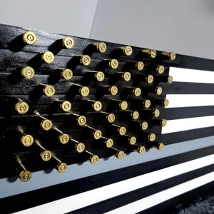 May include: A wooden American flag with black, white, and gray stripes. The stars are represented by brass bullet casings. The flag is mounted on a wall and is a unique piece of patriotic decor.