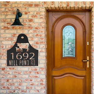 May include: Black metal house number sign with a cow and calf silhouette. The sign reads "1692 Mill Pond Rd."