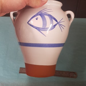 May include: White ceramic vase with a blue and white fish design. The vase has two handles and a brown base.