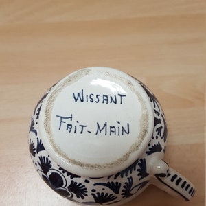 Pu&ograve; includere: Una tazza in ceramica bianca con un motivo floreale blu e bianco. Sul fondo della tazza &egrave; scritto "Wissant Fait-Main".