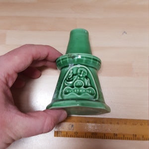Könnte beinhalten: Grünes Keramik-Dekorationsobjekt mit ausgestelltem Sockel und zylindrischem Oberteil. Das Stück hat ein geprägtes Design mit dem Text "HULSTKAMP" und der Nummer "1796". Das Stück ist etwa 7.6 cm hoch.