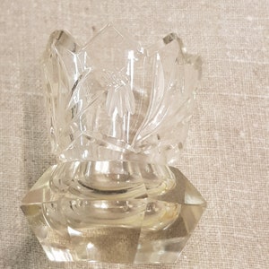 May include: A clear glass bud vase with a geometric base and a cut glass design. The vase is approximately 5 cm tall.