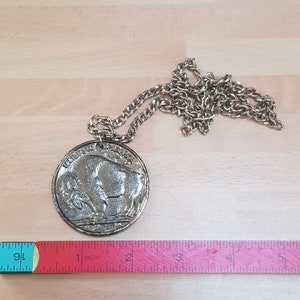 May include: A silver necklace with a round pendant featuring a buffalo design. The pendant is about 2 inches in diameter and has the words "United States of America" and "Five Cents" inscribed on it.