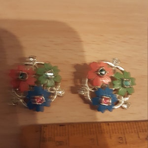 May include: Two gold-toned brooches with a floral design. Each brooch features three flowers in red, green, and blue with a rhinestone center.