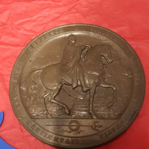 Puede incluir: Una medalla circular de bronce con una imagen en relieve de un hombre a caballo. La medalla tiene el texto "VICTORIA REGINA" y "GRATIA DEI" alrededor del borde. El texto "BRITANNIA" está en la parte inferior de la medalla.