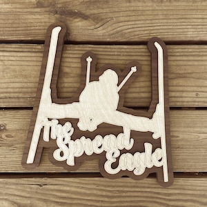 May include: Wooden wall art featuring a silhouette of a person skiing with the text "The Spread Eagle" in a decorative font.
