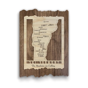 May include: A rectangular wooden wall plaque featuring a light-colored wood cutout of the state of Vermont layered over a dark wood backing. The map displays ski resort names marked with snowflake icons and the text "SKI VERMONT" and "The Mountains are Calling".