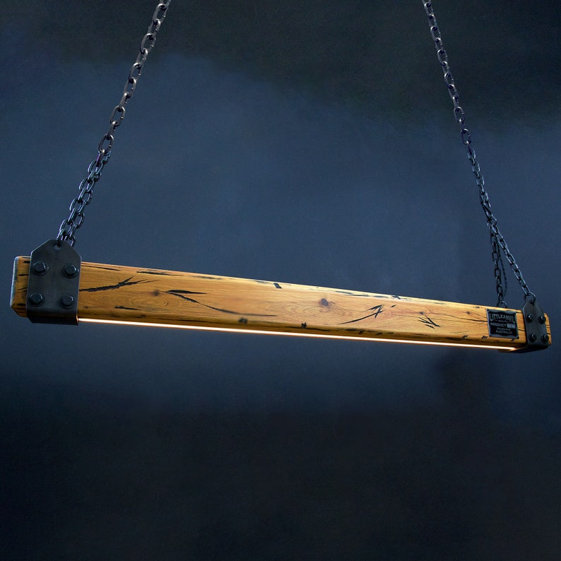 May include: A rustic wooden pendant light fixture with black metal chains and brackets. The wood has a natural grain pattern and is finished in a light brown color. The light fixture is suspended from the ceiling by two black chains.