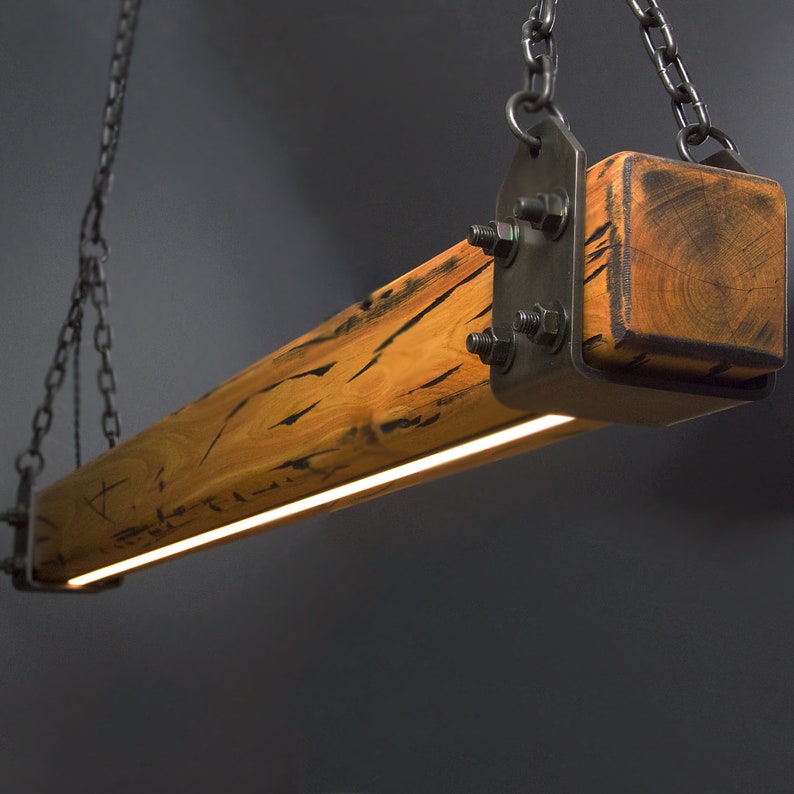 May include: A rustic wood and metal pendant light fixture with a warm, glowing light. The fixture is suspended from a chain and has a rectangular shape. The wood is a natural brown color with dark streaks, and the metal is a dark gray color.