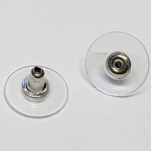 May include: Two clear plastic earring backs with a silver metal post. The backs are round and have a raised center.