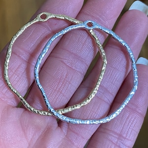 May include: Two metal hoops, one gold and one silver, with a textured finish. Both hoops have a small hole at the top.