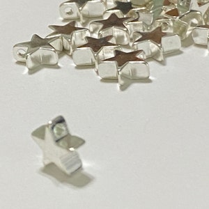 May include: A pile of silver star-shaped metal charms. The charms have a hole in the top for attaching to jewelry or other crafts.