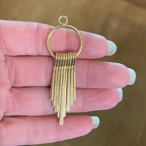 May include: Gold-toned pendant with a circular top and a fringe of thin, vertical bars hanging from the bottom.