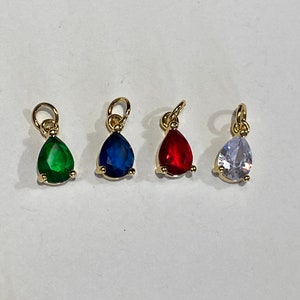 May include: Four teardrop-shaped charms with gold settings and different colored stones. The charms are green, blue, red, and clear.