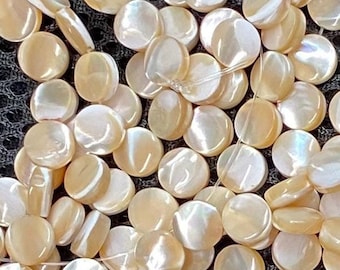 May include: A strand of iridescent white and beige round shell beads. The beads are strung on a clear thread and are arranged in a random pattern.