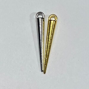 May include: Two metal cone-shaped charms with a loop at the top. One charm is silver and the other is gold.