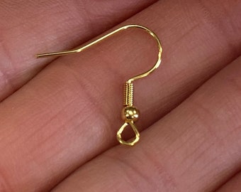 Puede incluir: Un gancho para pendiente de metal en tono dorado que presenta un alambre curvado, una pequeña espiral decorativa y una cuenta diminuta sobre un bucle circular en la base para sujetar componentes de joyería. Tiene un acabado pulido.