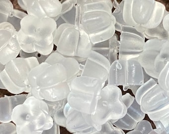 May include: A collection of small, translucent, frosted white plastic earring backs shaped like four-petaled flowers. These individual components are scattered in a cluster, each featuring a central hole for securing earring posts.