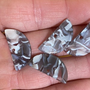 May include: Four half-circle shaped buttons with a white and gray marbled pattern. The buttons have a hole in the center.
