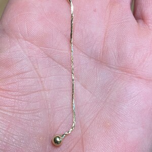 May include: A gold chain necklace with a small gold ball at the end.
