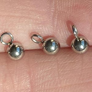 May include: Three silver-toned metal bead caps with a loop on top. The bead caps are round and have a shiny finish.