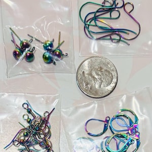 May include: A collection of iridescent rainbow-colored jewelry findings in clear plastic bags, including ball-post studs, hook ear wires, and lever-back earring components, displayed alongside a standard United States quarter coin for scale.