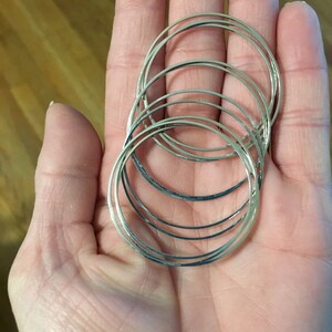 May include: A set of six silver-toned bangle bracelets stacked on top of each other. The bracelets are all the same size and have a smooth, polished finish.
