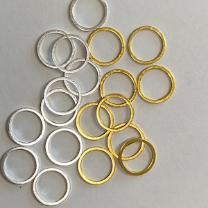May include: A collection of small, open metal rings in silver and gold tones. The rings are circular and appear to be made of a lightweight metal. The arrangement of the rings is scattered, with some overlapping. Ideal for jewelry making or craft projects.
