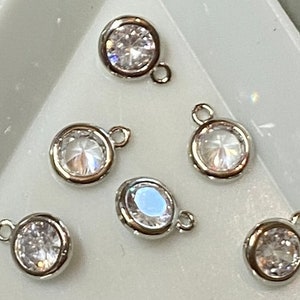 May include: Six silver-toned charms with clear crystal stones. Each charm has a loop for attaching to a bracelet or necklace.