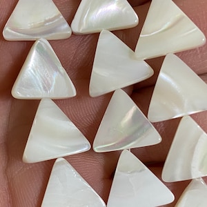 May include: A collection of white mother-of-pearl beads shaped as equilateral triangles. Each bead features a smooth, polished surface with a natural iridescent sheen that reflects light, showcasing the organic texture of the shell material.