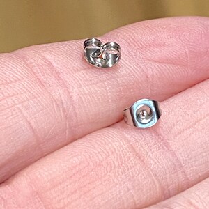 May include: Two silver earring backs, one with a flat back and the other with a curved back.