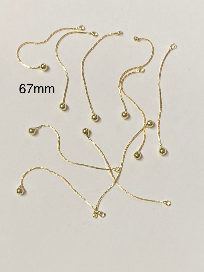 May include: A group of ten gold chain extenders with small round balls at the ends. Each extender measures 67mm in length.